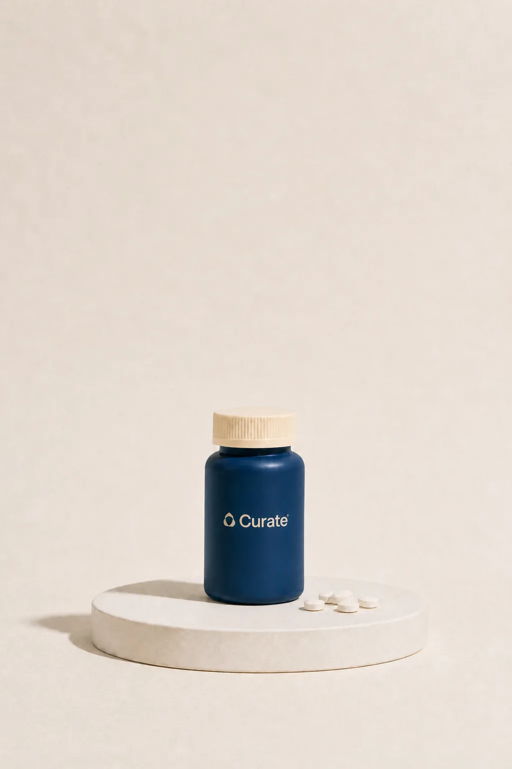 A navy Curate pill bottle with loose white tablets on a studio plinth