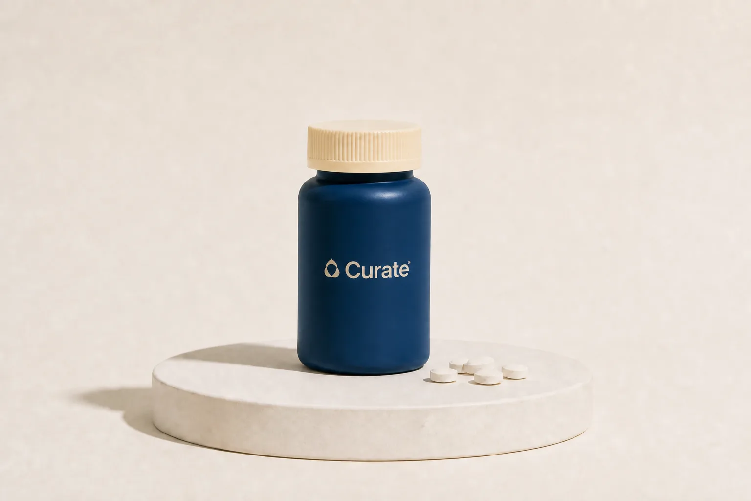A navy Curate pill bottle with loose white tablets on a studio plinth