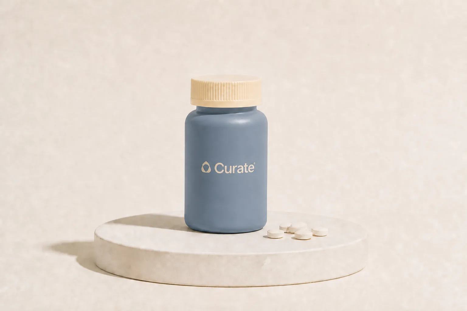 A slate-blue Curate pill bottle with loose white tablets on a studio plinth